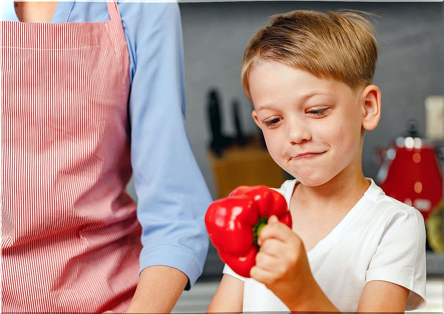 Child with a red pepper in the kitchen.