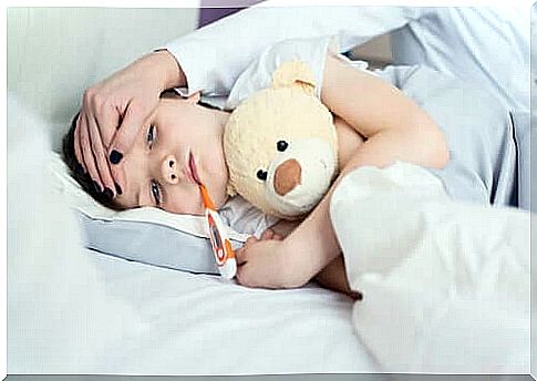 A young boy in bed, with a thermometer in his mouth. 