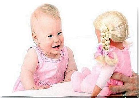 A little girl laughs in front of a doll