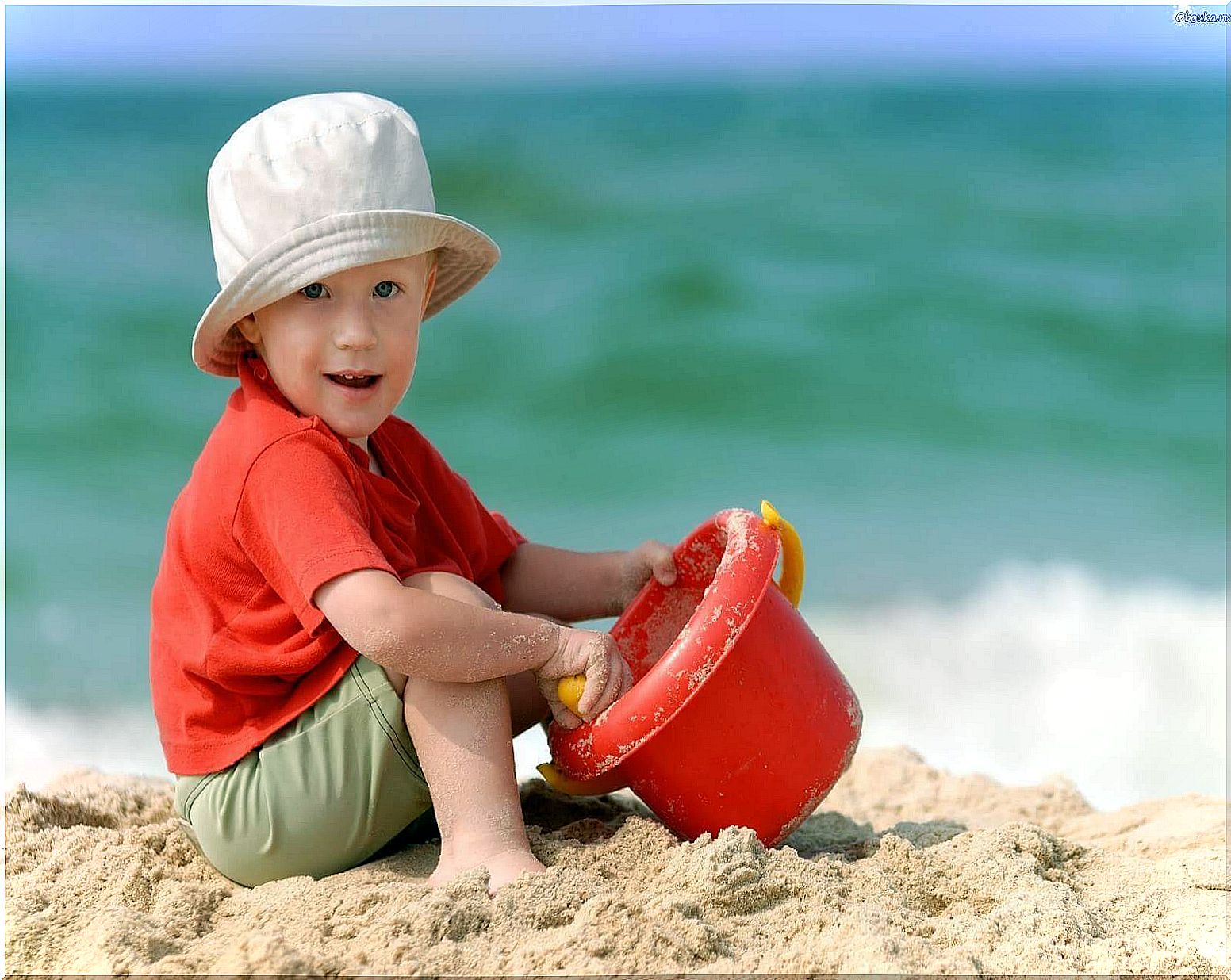 Child at the beach in the sand, in creative play with a bucket